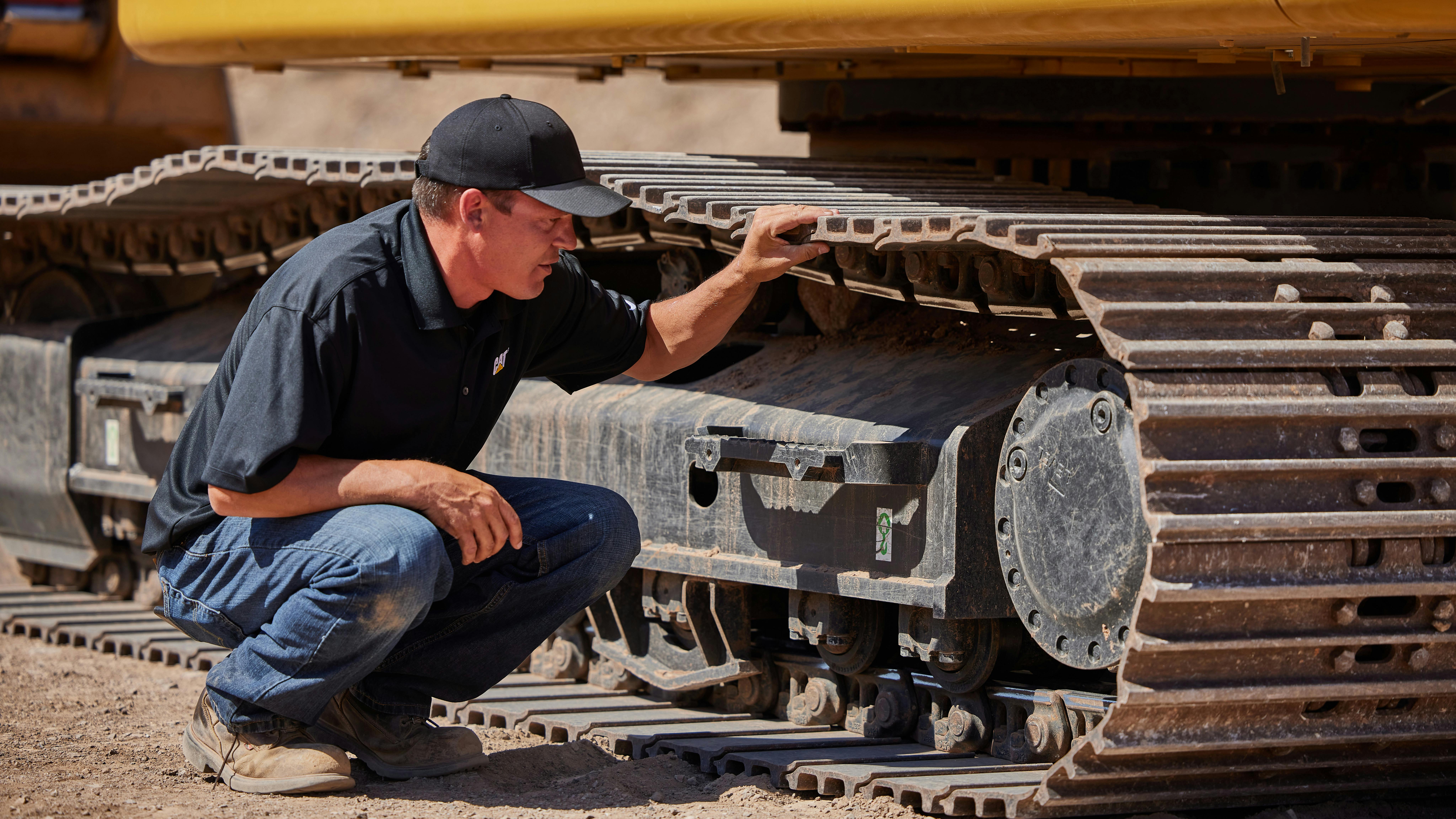 An operator inspects a Caterpillar 320 HEX undercarriage.