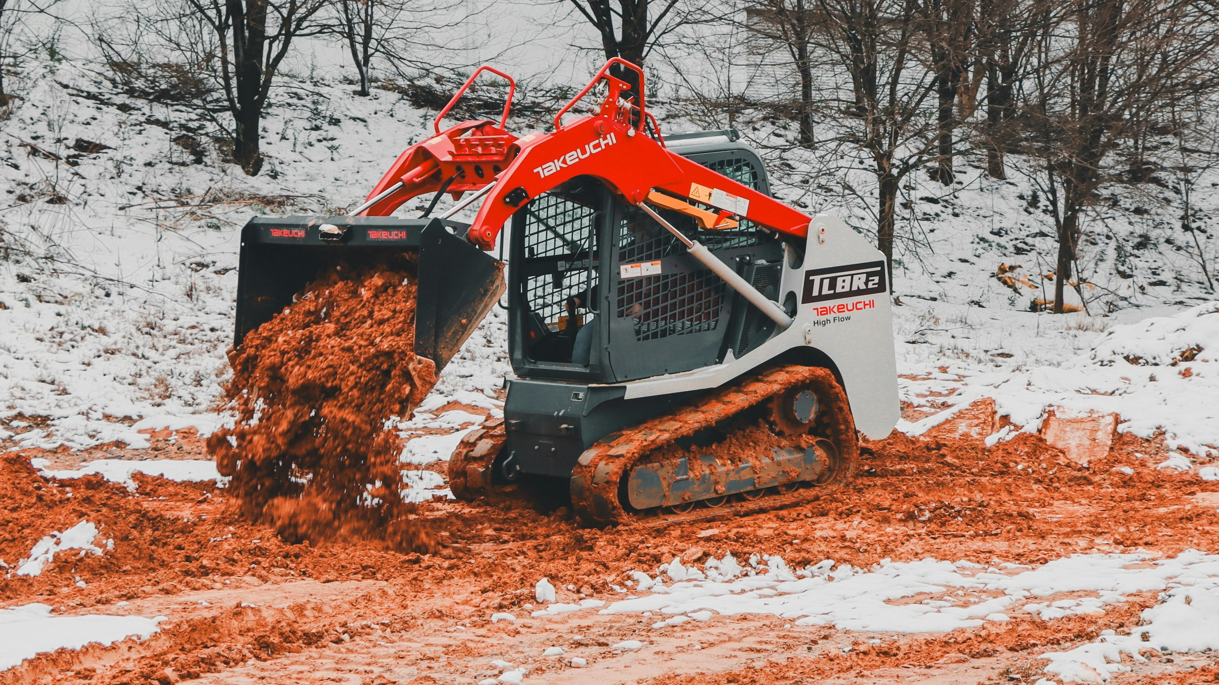 A Takeuchi compact track loader dumping mud in the winter snow.