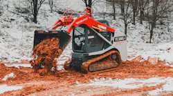 A Takeuchi compact track loader dumping mud in the winter snow.