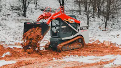 A Takeuchi compact track loader dumping mud in the winter snow.