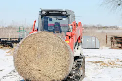 A Takeuchi compact track loader carrying a bale of hay.